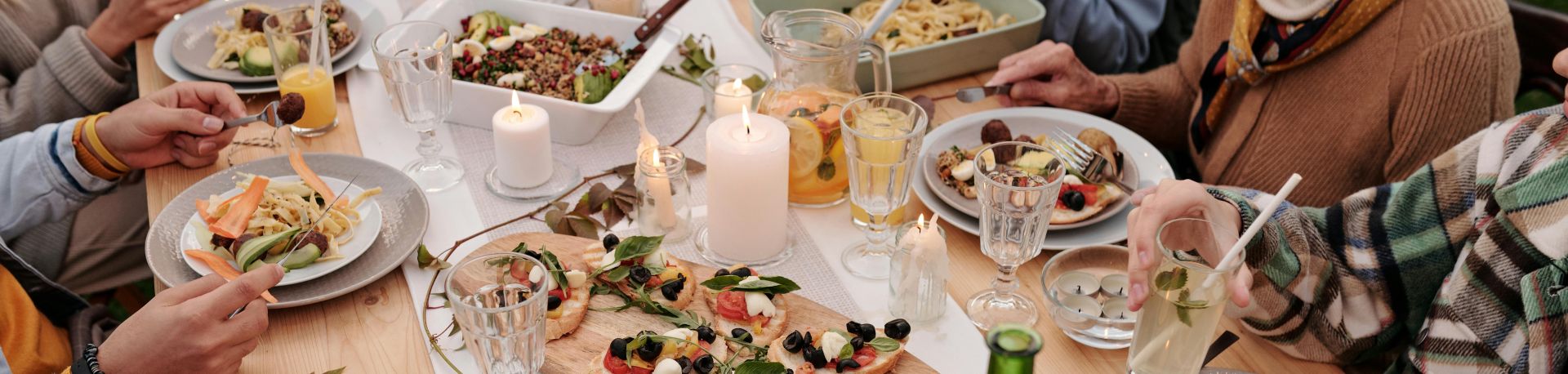 From above crop people enjoying festive dinner with snacks at garden table with candles burning