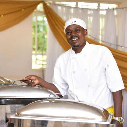 A cheerful chef stands by chafing dishes in a Nairobi hotel buffet setting.